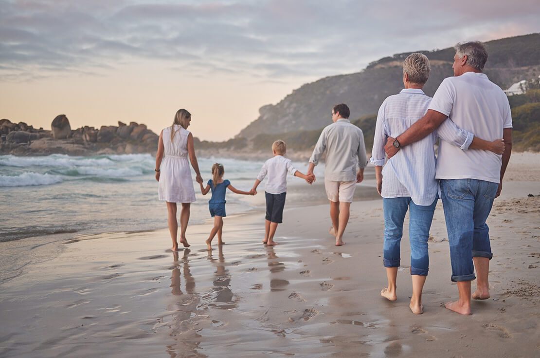 Rear view of Multi generation family holding hands and walking along the beach together. Caucasian family with two children, two parents and grandparents enjoying summer vacation